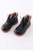 A pair of black faux leather booties with lace-up fronts and brown soles. Aaria Tees