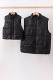 Two black puffer vests hanging on a rack against a white background Aaria Tees