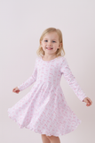 Young girl wearing a pink dress with a subtle pattern on a white background Aaria Tees