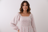 Woman wearing a white dress with floral patterns against a plain background Aaria Tees